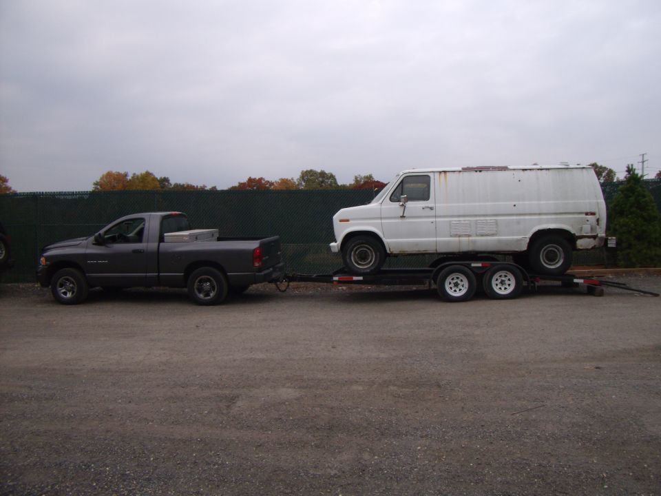 Gray Dodge Ram 1500 towing a white van on a trailer, side view