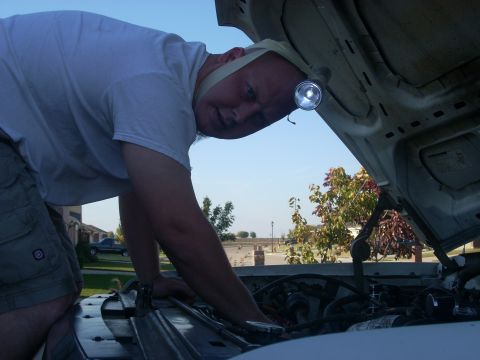 1992 Ford Bronco - Man works on car engine under open hood, illuminated by a headlamp.