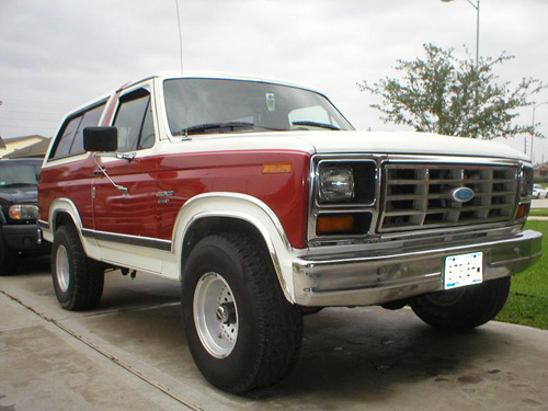 Red and white Ford Bronco, 3/4 front view. Another dark SUV is parked to the left
