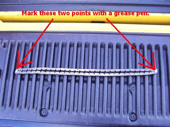Timing chain laid across a blue truck bed, with red arrows pointing to its ends and text instructing to mark two points with a grease pen