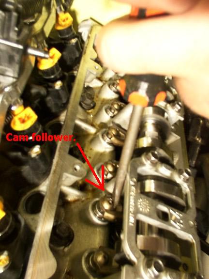2007 Ford Mustang - Screwdriver being used to adjust a cam follower in an engine's valve train.