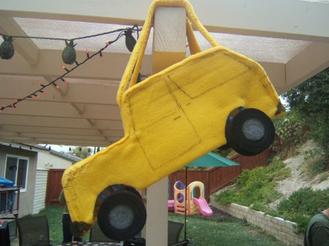 1988 Ford Bronco - A handmade yellow felt toy truck is suspended from a wooden beam in a backyard setting.
