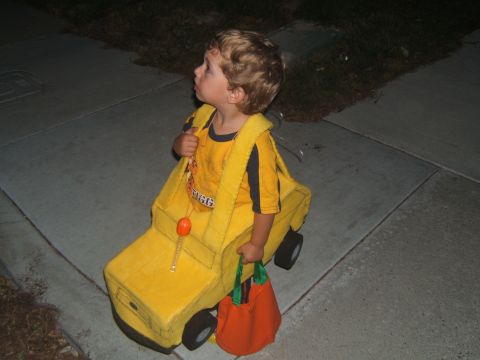 1988 Ford Bronco - A young child dressed as a yellow school bus walks along a sidewalk at dusk.
