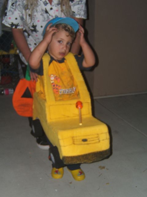 1988 Ford Bronco - A child dressed in a yellow school bus costume, complete with a pumpkin trick-or-treat bag, stands on a paved surface.
