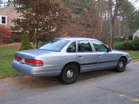 1991 Ford LTD Crown Victoria - A light blue sedan is parked on a residential street with trees and a house in the background.