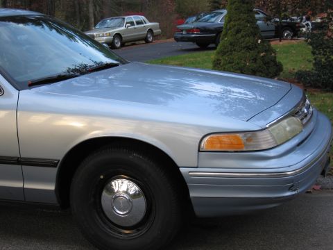 1991 Ford LTD Crown Victoria - A light blue sedan is parked in a driveway with other vehicles visible in the background.