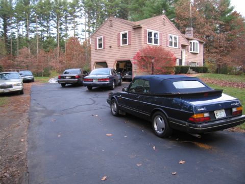 1991 Ford LTD Crown Victoria - A dark blue Saab 900 Turbo convertible is parked in a driveway next to a house with several other vehicles.