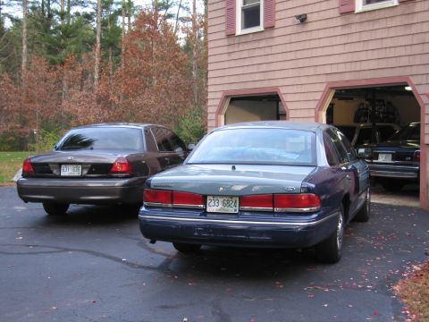 1991 Ford LTD Crown Victoria - A pair of Ford Crown Victorias are parked outside a suburban garage on an autumn day.