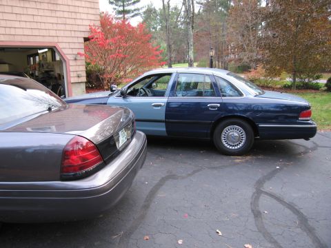 1991 Ford LTD Crown Victoria - A gray Ford Crown Victoria is parked in front of a blue and light blue Ford Crown Victoria in a driveway.