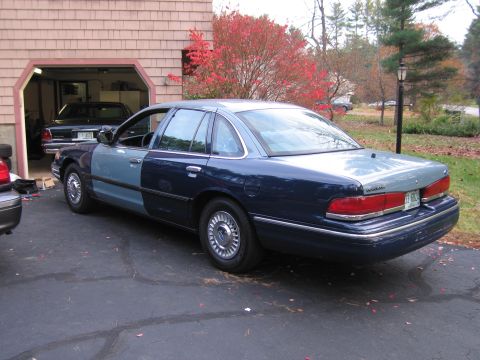 1991 Ford LTD Crown Victoria - A two-tone Ford Crown Victoria is parked in a driveway next to a garage, with another car visible inside.