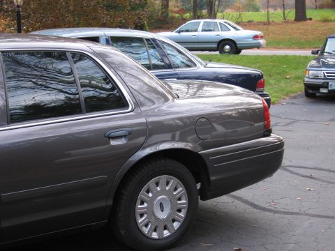 1991 Ford LTD Crown Victoria - Rear quarter panel of a dark grey 1991 Ford Crown Victoria LTD, parked in a driveway with other vehicles.