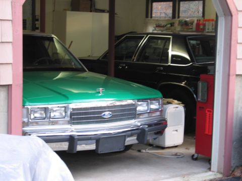 1991 Ford LTD Crown Victoria - The front of a green 1991 Ford Crown Victoria is visible, parked in a garage with another car behind it.