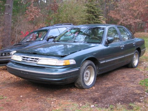 1991 Ford LTD Crown Victoria - A dark green sedan sits in a driveway with a blue SUV behind it, both appearing to be for sale.