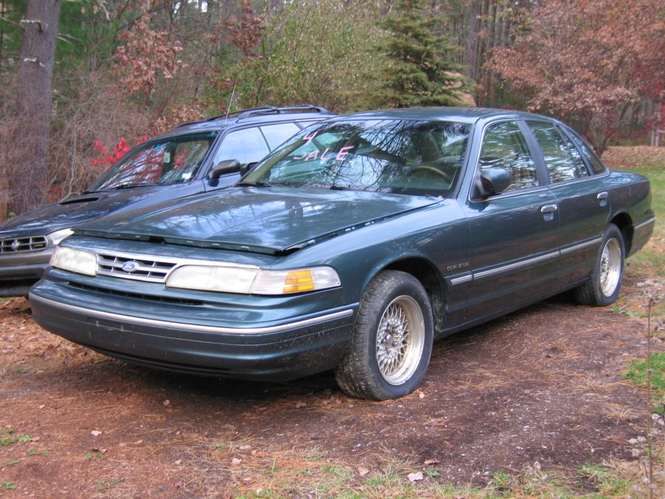 Dark green sedan with hood ajar, parked next to a blue SUV. "SALE" sign visible on windshield