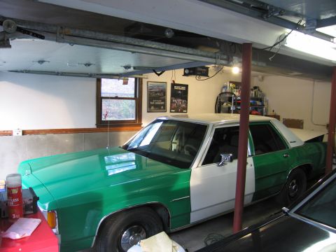 1991 Ford LTD Crown Victoria - A two-tone green and white sedan is parked in a garage, with another vehicle partially visible in the foreground.