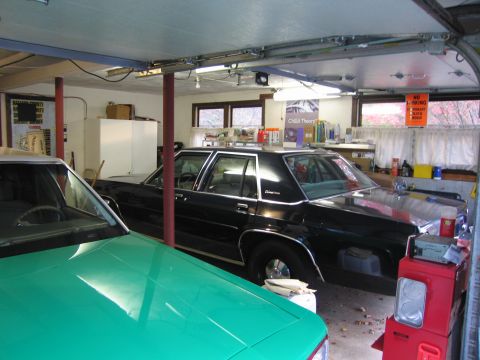 1991 Ford LTD Crown Victoria - Two cars are parked inside a garage, with shelves and various items in the background.