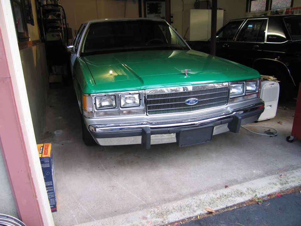 Green Ford Crown Victoria with chrome grille and bumper, parked in a garage. Front view