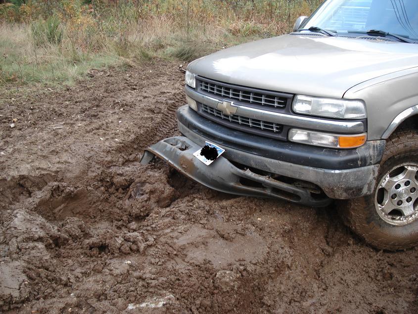 Silver Chevrolet pickup truck stuck in mud, front bumper damaged