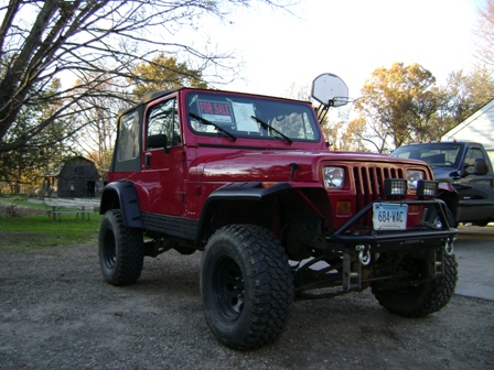 1996 Ford Bronco - A red Jeep Wrangler is parked in a gravel lot with a "FOR SALE" sign in the window.