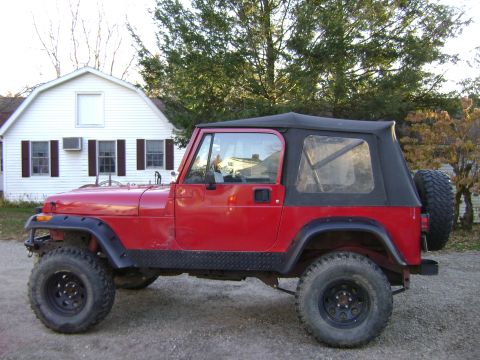 1996 Ford Bronco - A red Jeep Wrangler is parked in front of a white house with a black soft top and spare tire mounted on the rear.