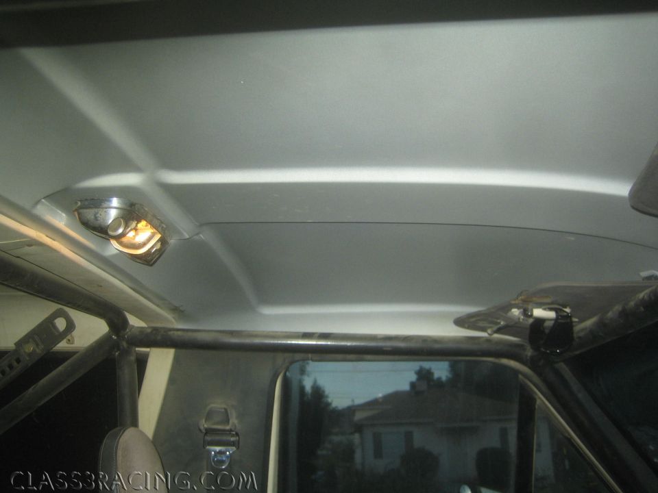 Vehicle interior showing headliner, roll cage, rear window and dome light with houses outside