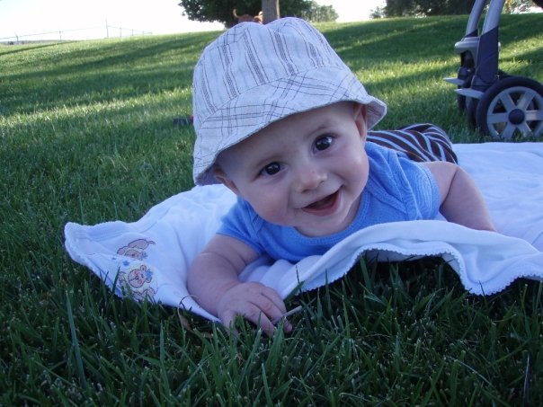 Baby wearing a bucket hat lies on a white blanket on grass
