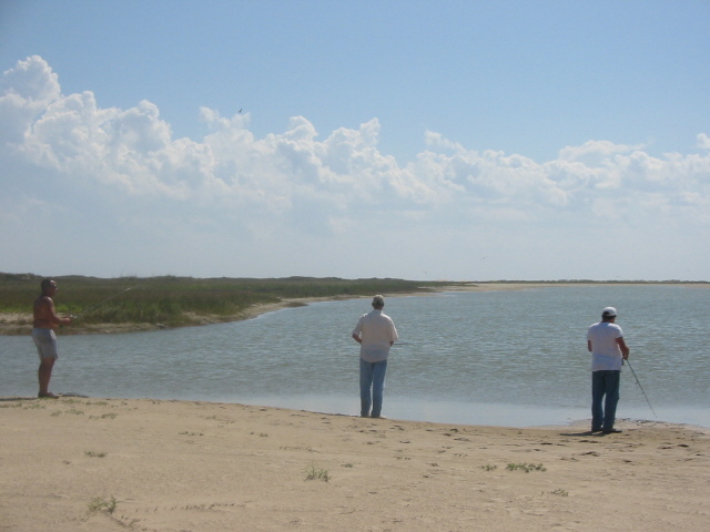 Three men fishing on a beach with a calm body of water and cloudy sky