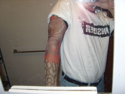 1989 Ford Bronco - A man's reflection shows his heavily tattooed arm and a t-shirt with a distressed graphic design.