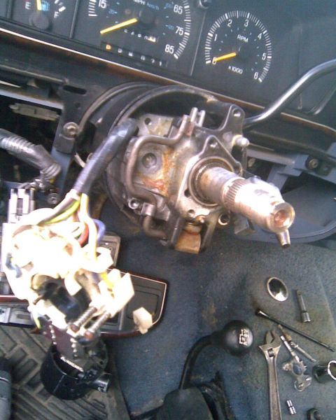 1989 Ford Bronco - Steering column torn down inside a truck cab: the wheel and upper shrouds are off, exposing the greasy cast housing, splined shaft end and…