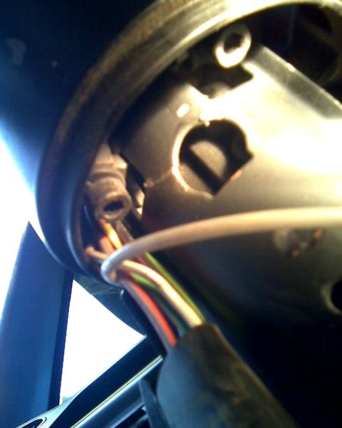 1989 Ford Bronco - Extreme close-up looking up under a steering column with the lower shroud removed, showing the bare metal column tube, a rubber grommet, an…