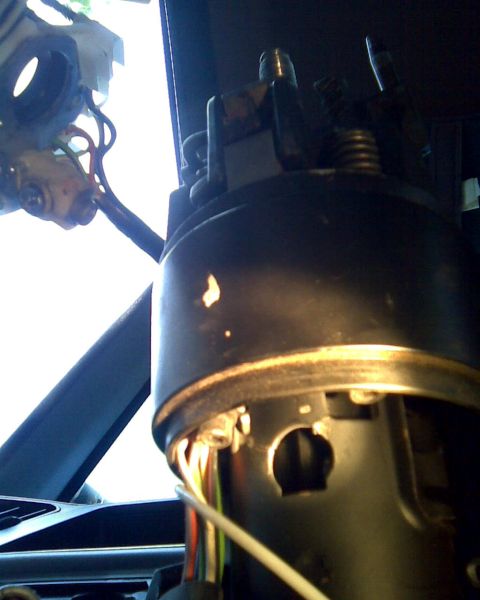 1989 Ford Bronco - Backlit interior close-up of a steering column with the shroud partly removed, showing the black column housing, exposed lock cylinder cuto…