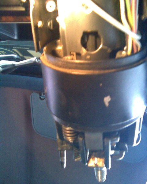 1989 Ford Bronco - Close-up of a partly disassembled steering column inside a vehicle, with the outer tube pulled down to expose the internal shift linkage, c…