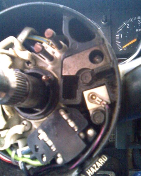 1989 Ford Bronco - The interior of a vehicle's steering column shows electrical components and wiring, with a tachometer in the background.
