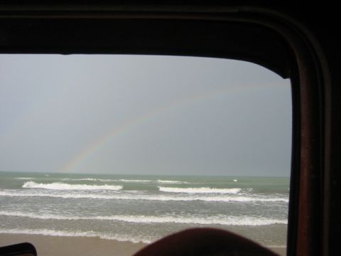 1984 Ford Bronco - A rainbow arcs over the ocean as seen from inside a vehicle.