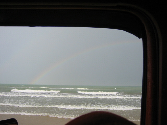 view of ocean waves and a rainbow through a window frame