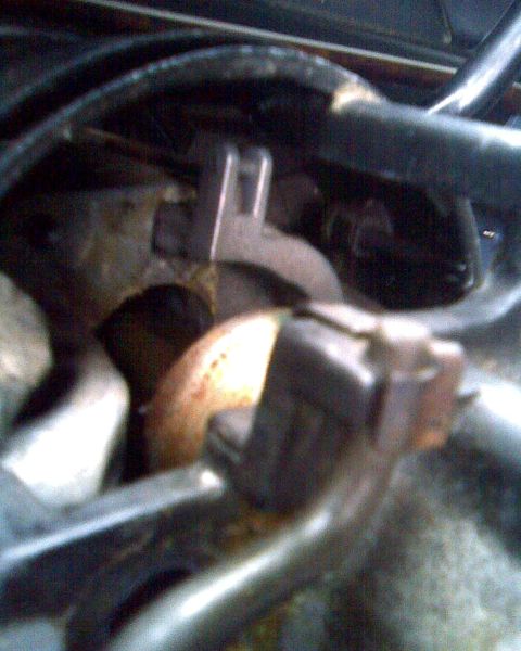 1989 Ford Bronco - Out-of-focus close-up under the dash or in an engine bay showing a stamped steel bracket with a slotted tab, surrounded by rubber hoses, ru…