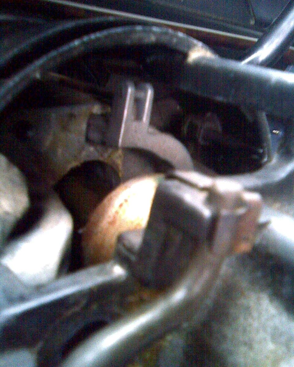 Blurry close-up of a stamped steel bracket among hoses and rusty hardware