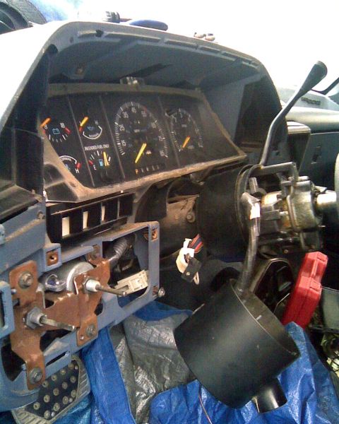 1989 Ford Bronco - A gutted Ford truck dash assembly resting on a blue tarp during removal, with the instrument cluster still in place showing fuel, temperatu…