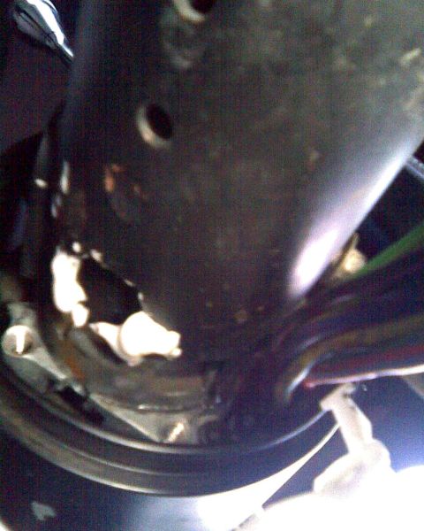 1989 Ford Bronco - Dark, blurry close-up looking up a steering column shaft inside a vehicle, showing the bare metal tube with mounting holes and the wiring h…