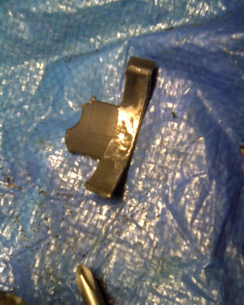 1989 Ford Bronco - Close-up of a damaged metal bracket resting on a blue tarp, with a screwdriver tip in view.