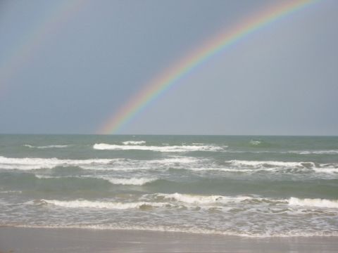 1984 Ford Bronco - A rainbow arcs over the ocean waves on a cloudy day at the beach.