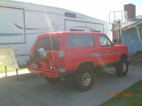 1985 Ford Bronco - This red 1985 Ford Bronco is parked in front of a large RV and a house.