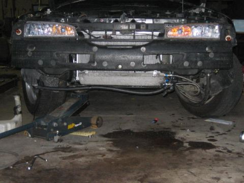 1996 Ford Thunderbird - The front of a 1996 Ford Thunderbird is shown with its bumper removed and engine exposed, supported by a jack.