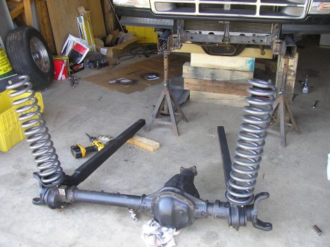 1996 Ford Bronco - The front axle and suspension components are laid out on the garage floor, with the vehicle elevated on jack stands.
