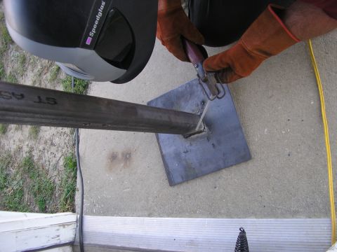 1996 Ford Bronco - A person in welding gear is attaching a metal pipe to a square base plate.