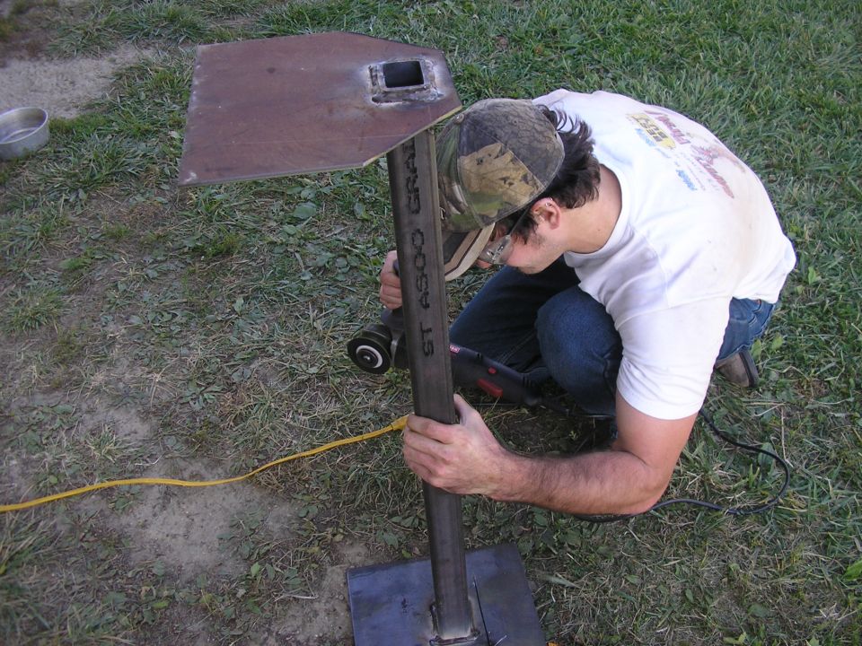 Man in camouflage hat grinds metal post with "ST A500 GRA" visible