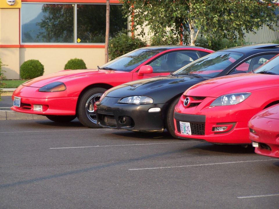 Red Mitsubishi 3000GT, dark gray Mitsubishi Eclipse, and red Mazda 3 parked in a lot.