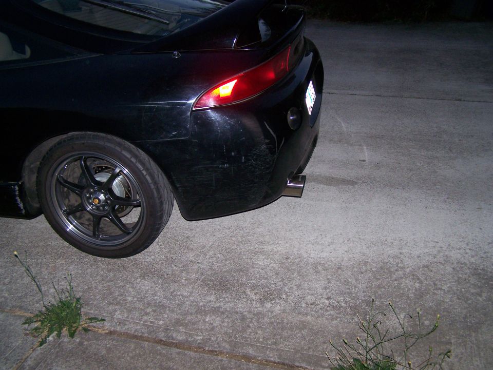 Black car's rear quarter panel, wheel, and exhaust tip.
