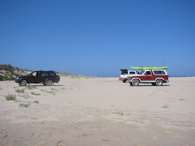 1984 Ford Bronco with kayak on roof and another SUV on beach