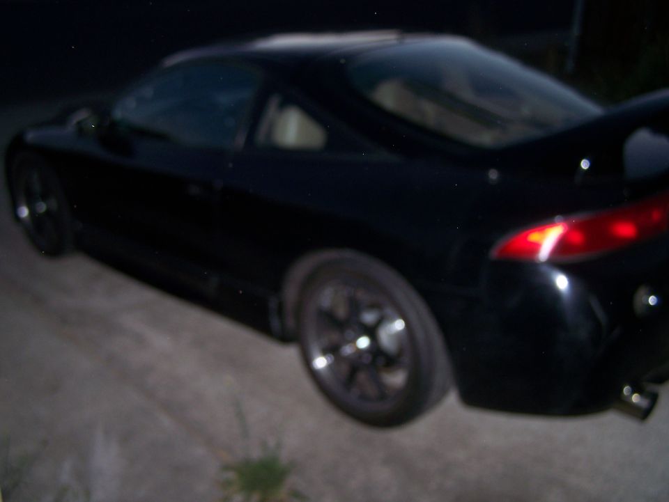 Black coupe with spoiler and red taillight, rear driver's side view.